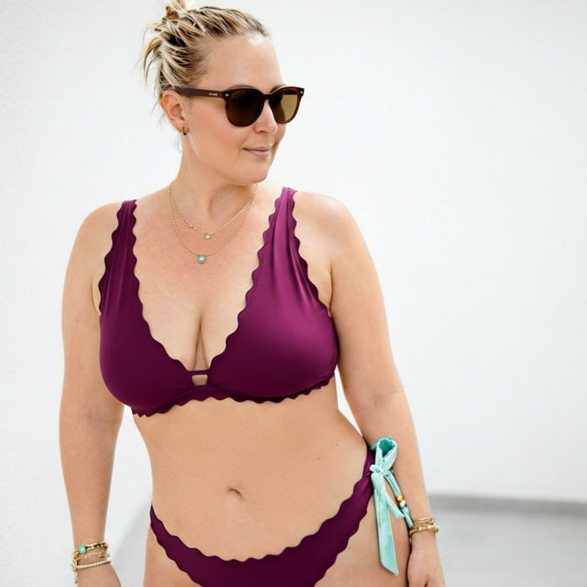 Woman wearing a purple bikini with sunglasses on a plain background